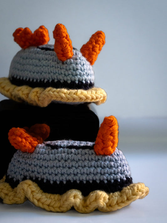Hand-crocheted blue-grey nudibranch with orange rhinophores and yellow frill